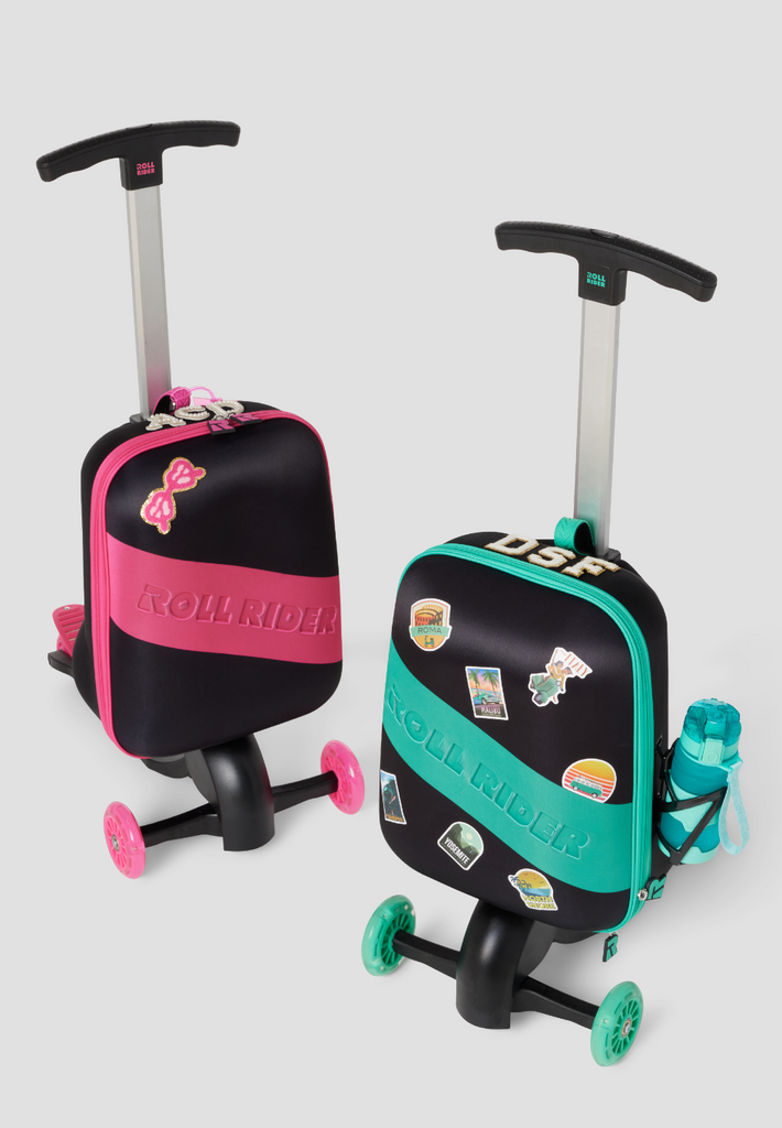 Overhead angle of a pink and a green Roll Rider scooter suitcase side-by-side with stickers on them on a white background. 